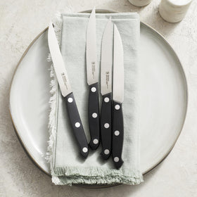 Henckels Prime steak knife set with black handles shown in a balanced grip for comfortable cutting.