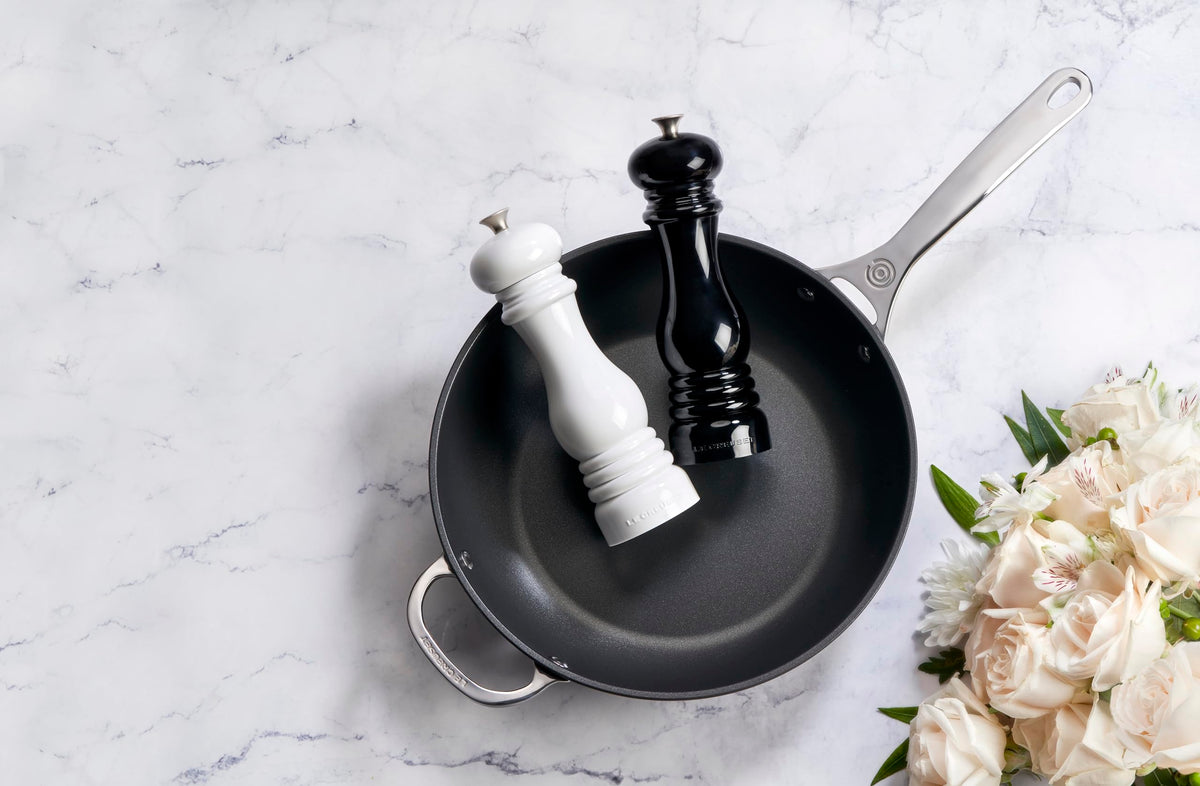 Le Creuset salt and pepper mills shown on a kitchen counter for daily use.
