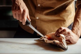 Mercer Culinary Millennia boning knife on cutting board for meat separation.