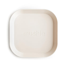 Mushie square ivory plates with child hands ready for mealtime