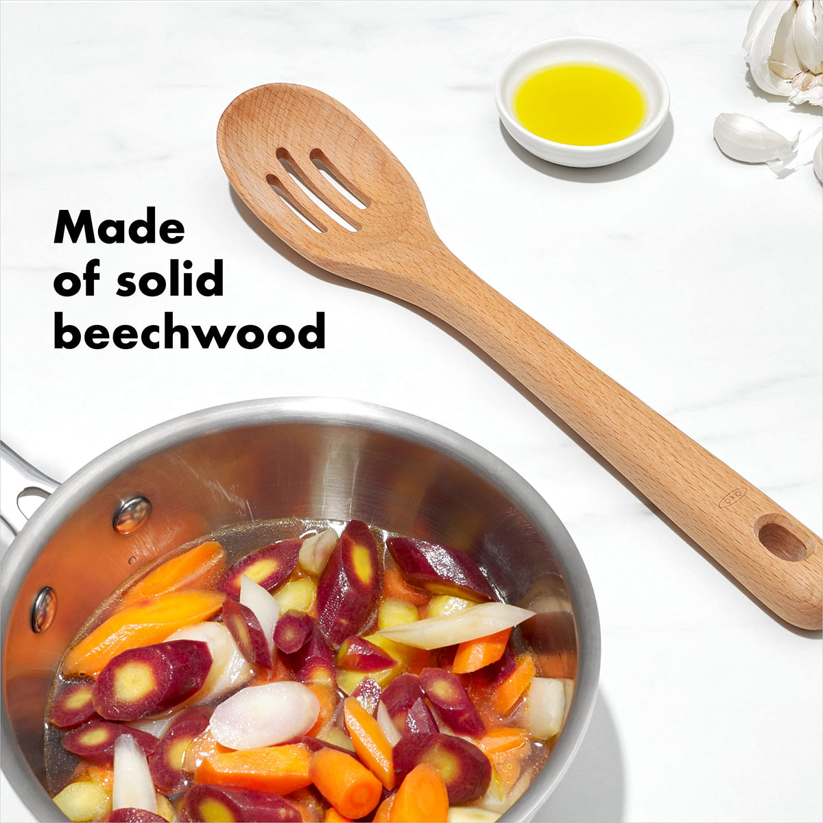OXO Good Grips wooden slotted spoon draining liquids during cooking.