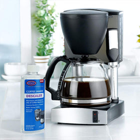 Urnex bottle beside coffee beans communicates home-use maintenance.